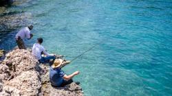 3 people rock fish over calm blue waters 