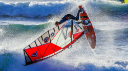 Windsurfing contestant attempting a manouvere. Their body is parallel to the waves, their board perpendicular to gravity